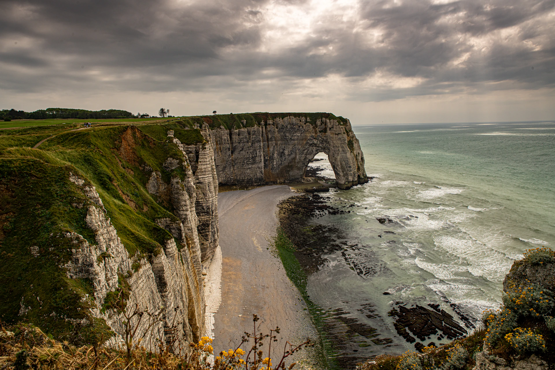 a rocky cliff with a beach below it under a cloudy sky