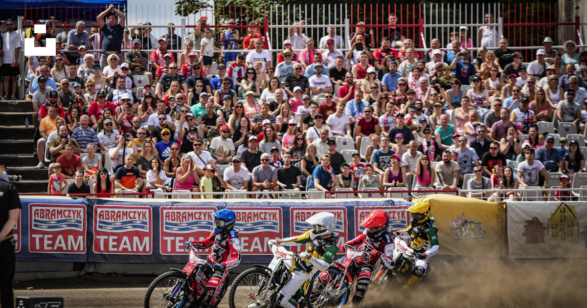 A group of motorcyclists racing around a track in front of a crowd ...