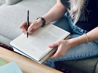 a woman sitting on a couch writing on a notebook