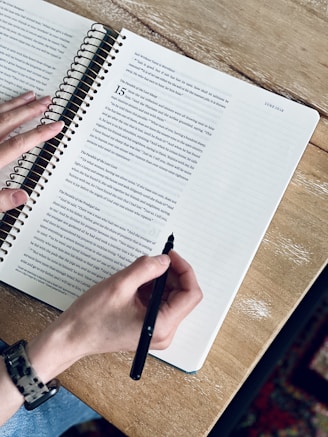 a person writing on a notebook with a pen