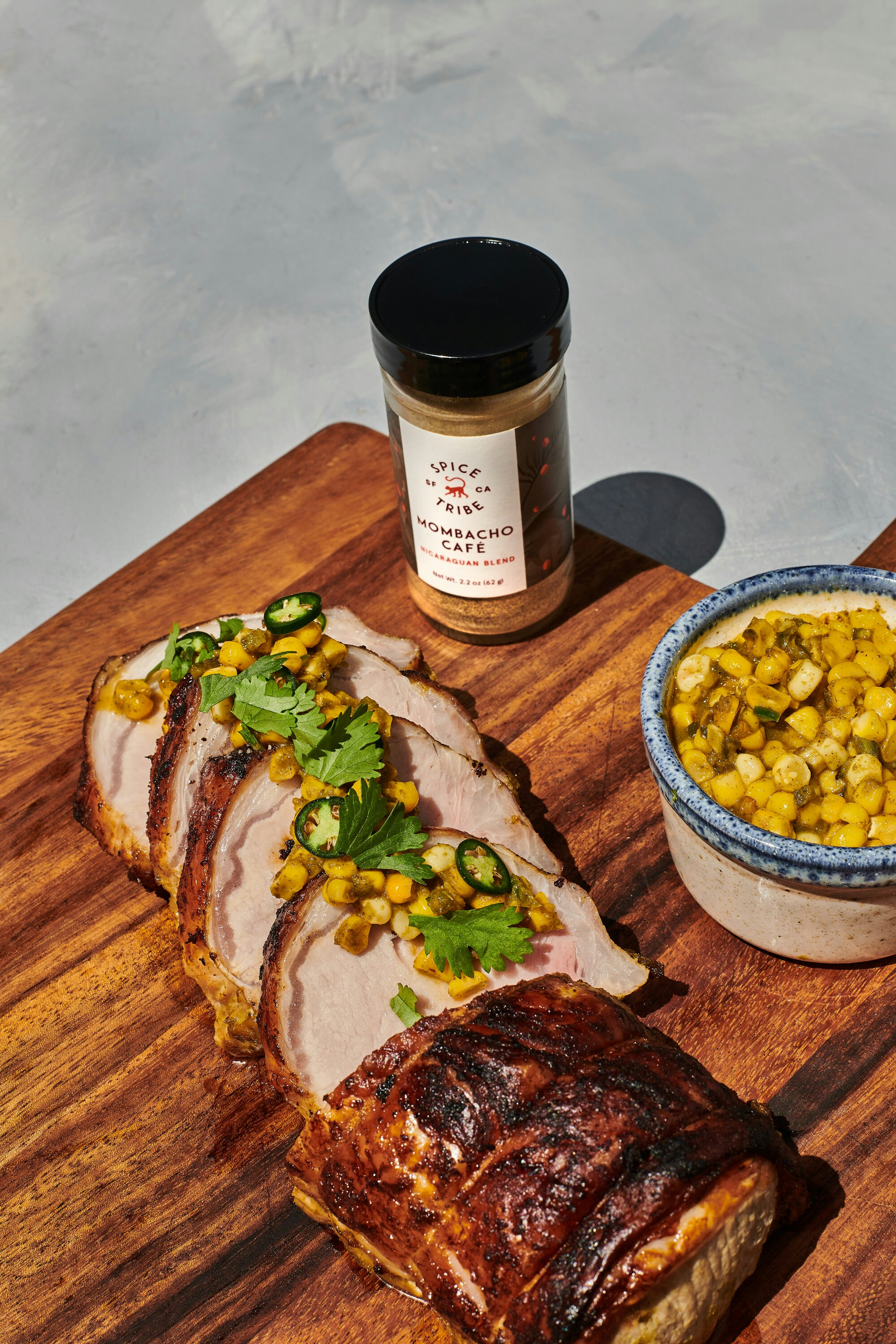 A wooden cutting board topped with sliced meat next to a bowl of corn ...