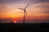 the sun is setting behind a wind farm