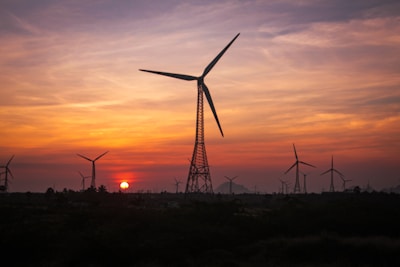 the sun is setting behind a wind farm