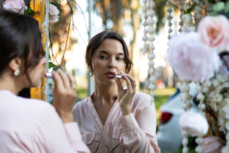 a woman is putting on lipstick while another woman looks on
