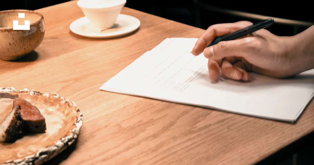A person sitting at a table writing on a piece of paper photo – Free ...