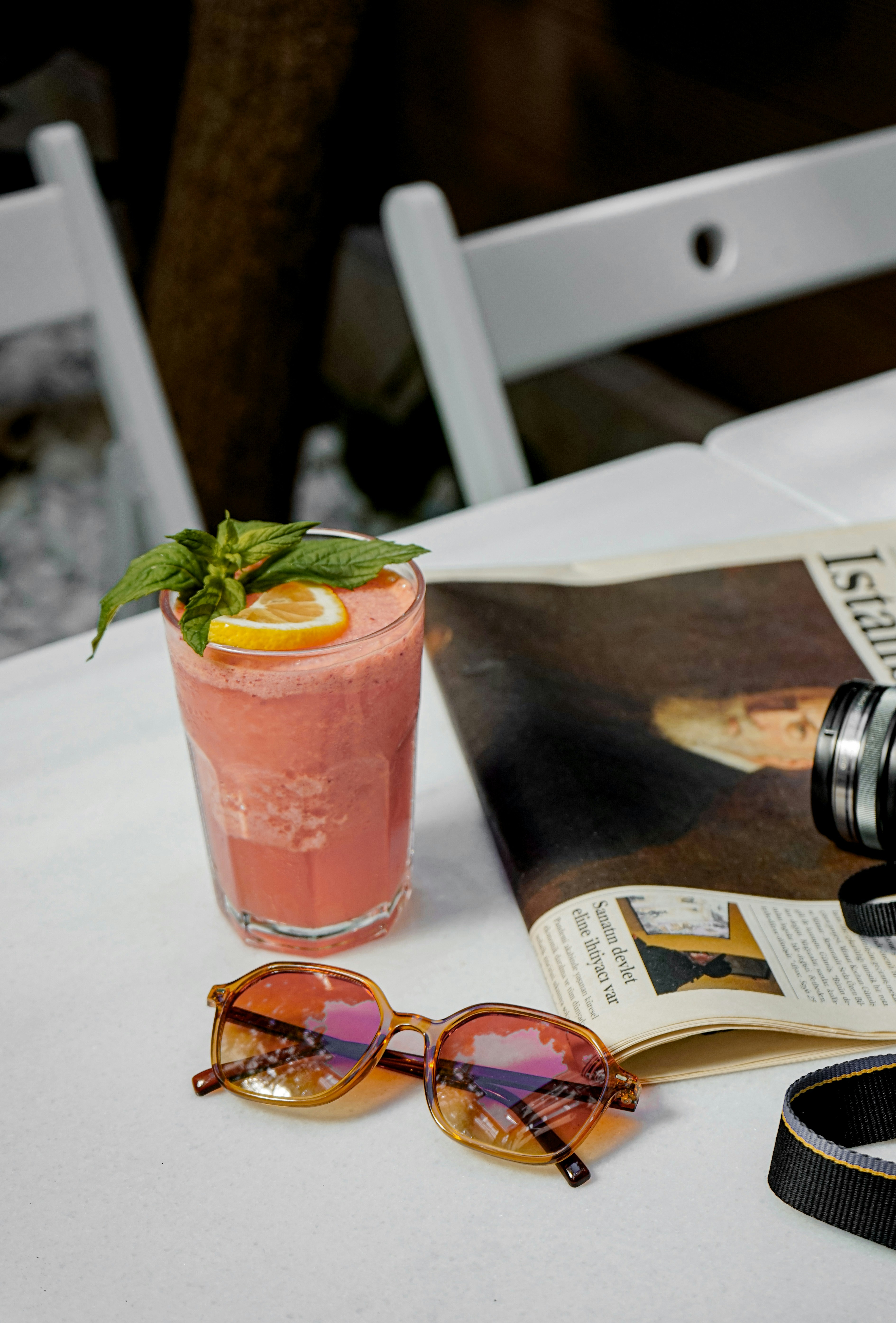 uma revista, óculos escuros e uma bebida sobre uma mesa