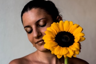 a woman holding a sunflower up to her face