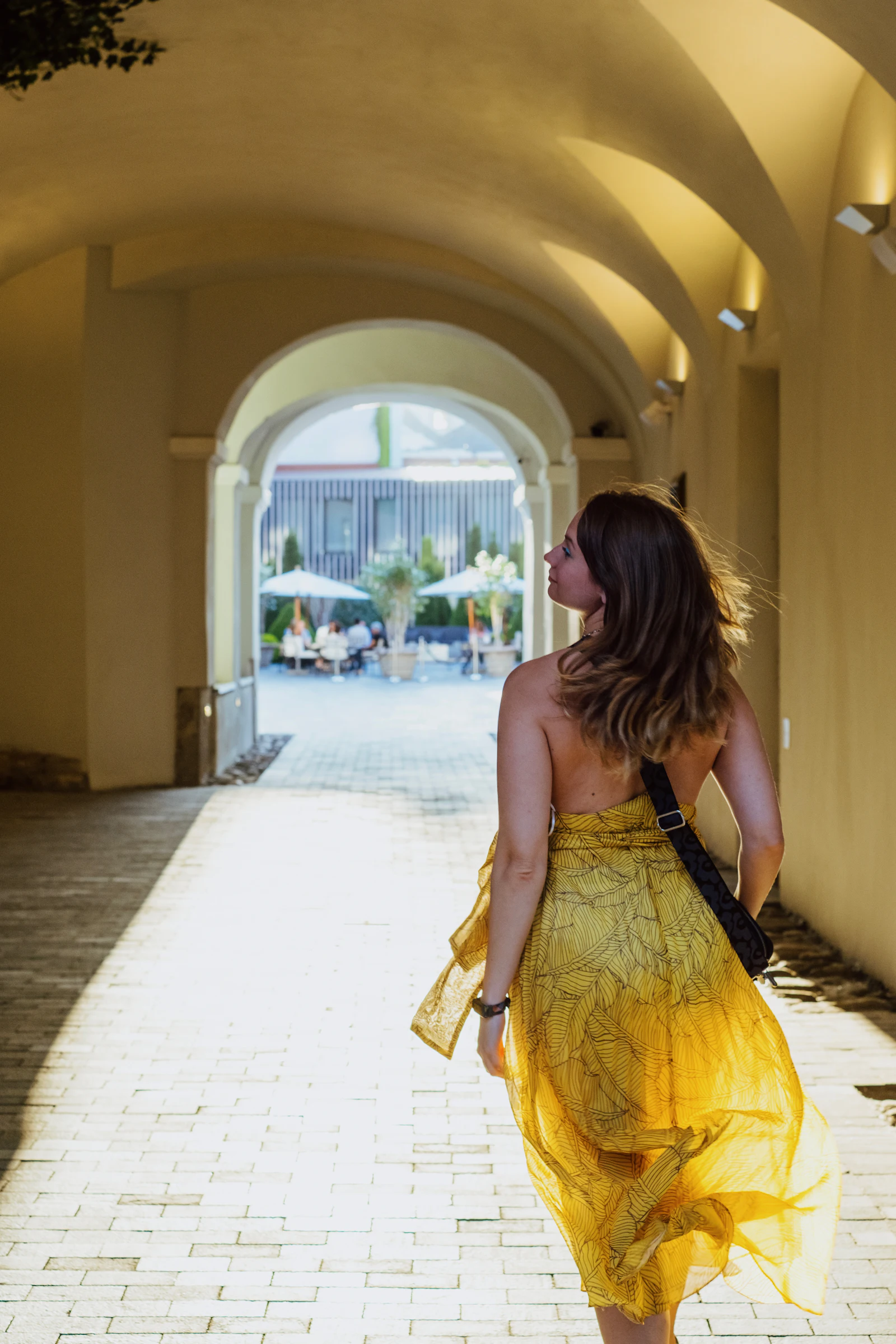 Woman walking under arches in a flowing mango yellow maxi dress