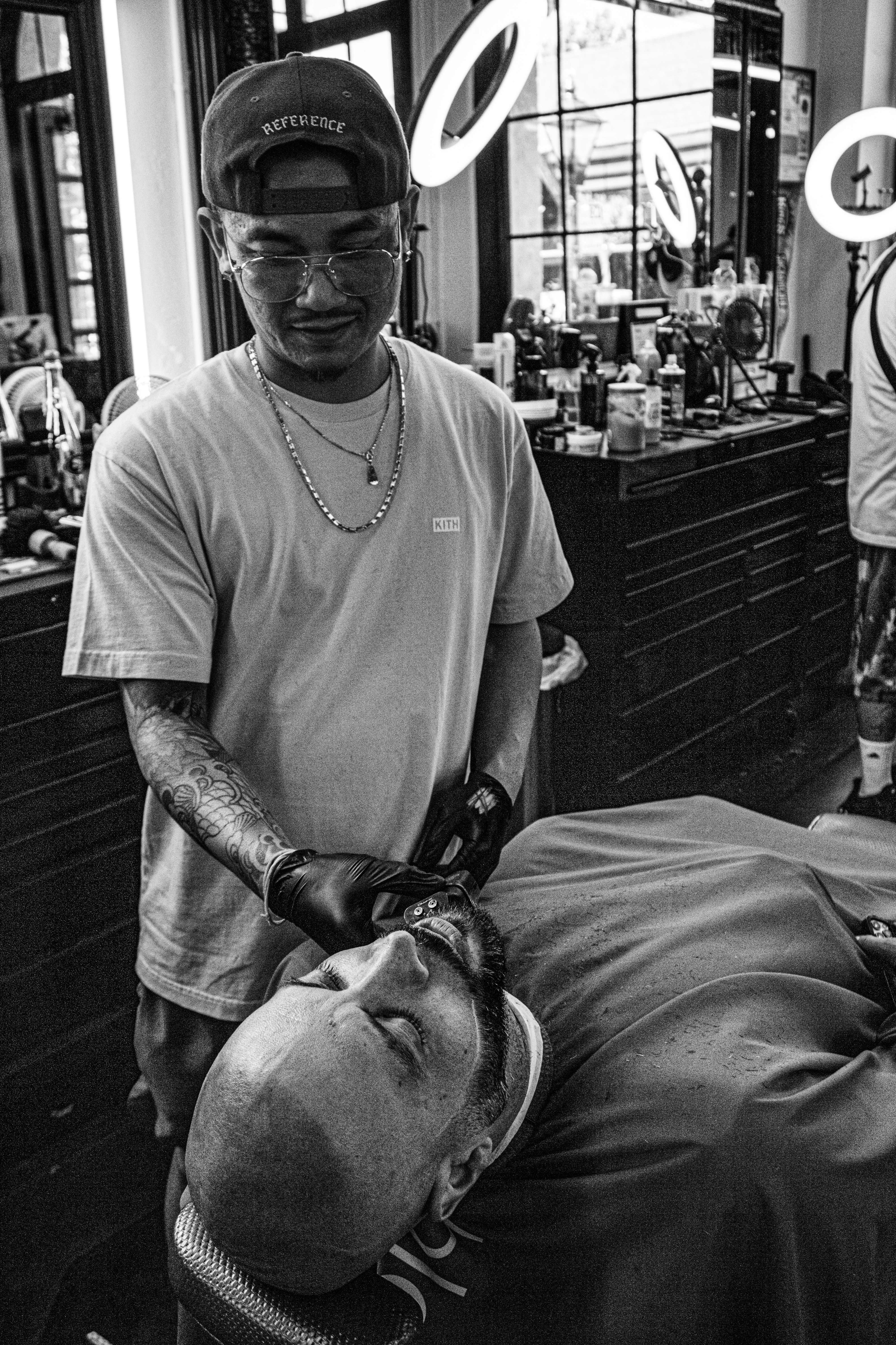 Tunde Afolabi, senior barber at DY Cutz, working with precision on a client beard, dark barbershop ambiance