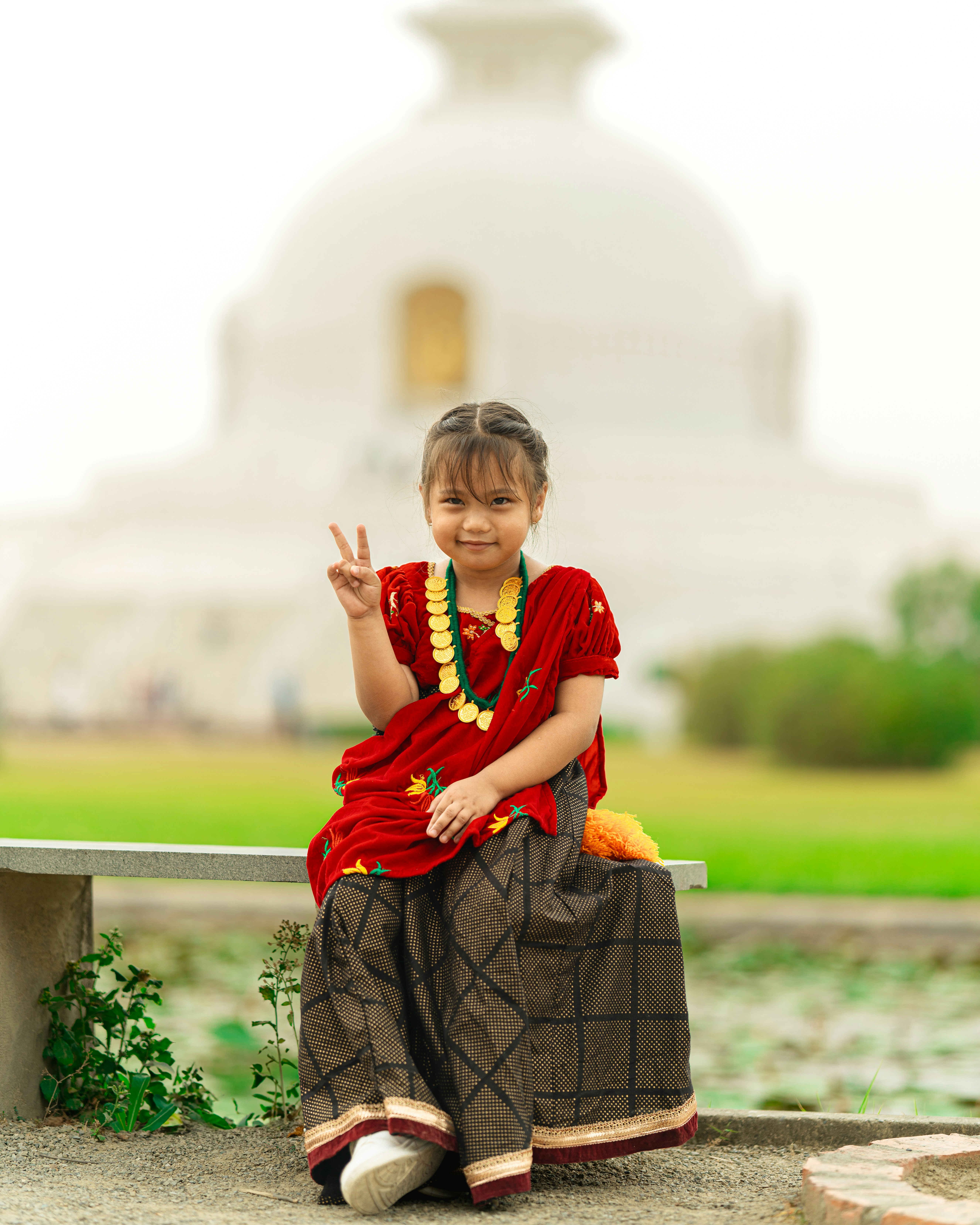 a little girl sitting on a bench making a peace sign