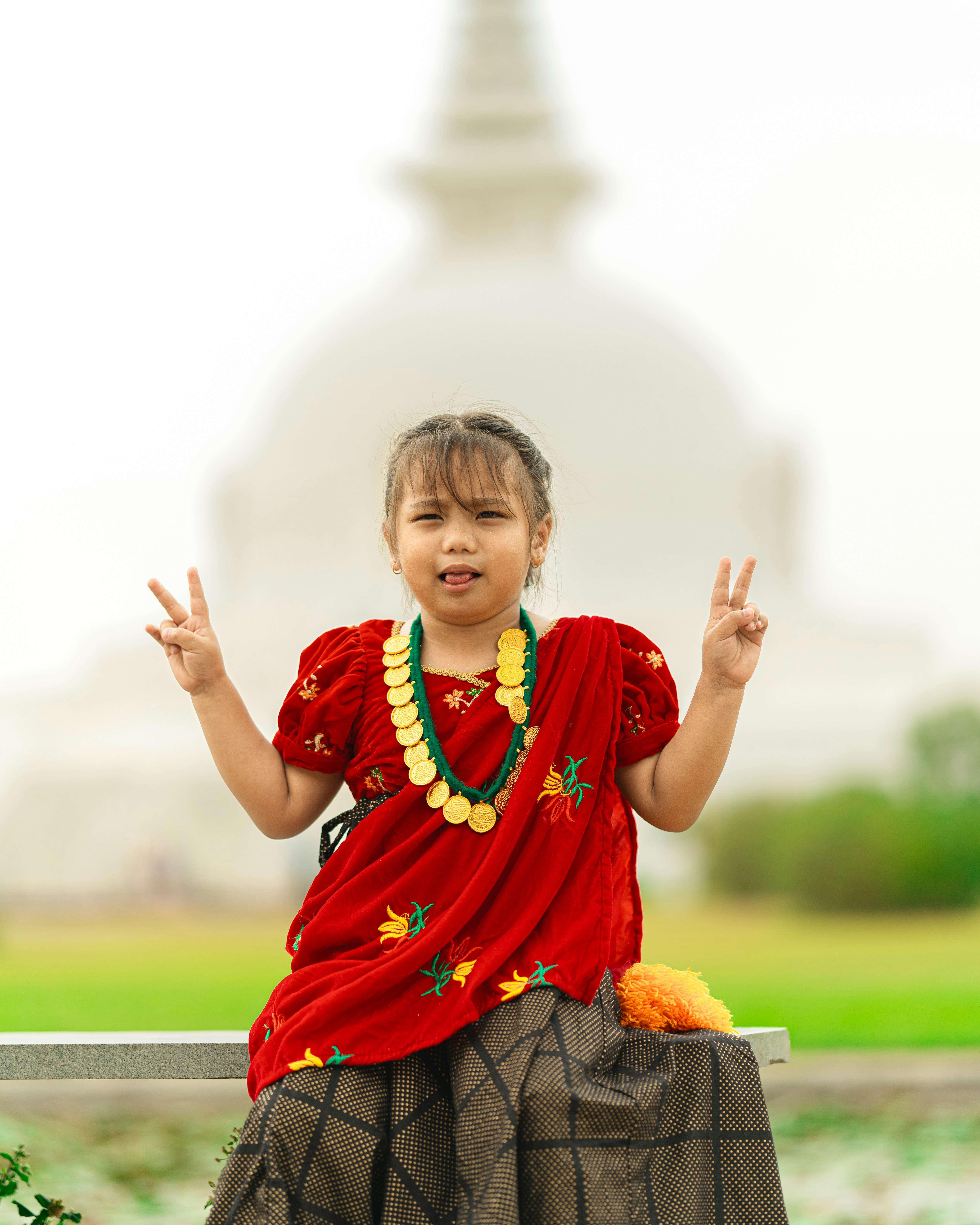 a little girl sitting on a bench making a peace sign