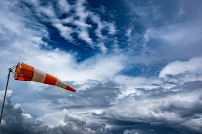 an orange and white flag on a pole under a cloudy sky