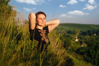 a woman standing in tall grass with her arms behind her head