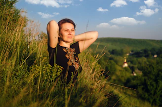 a woman standing in tall grass with her arms behind her head