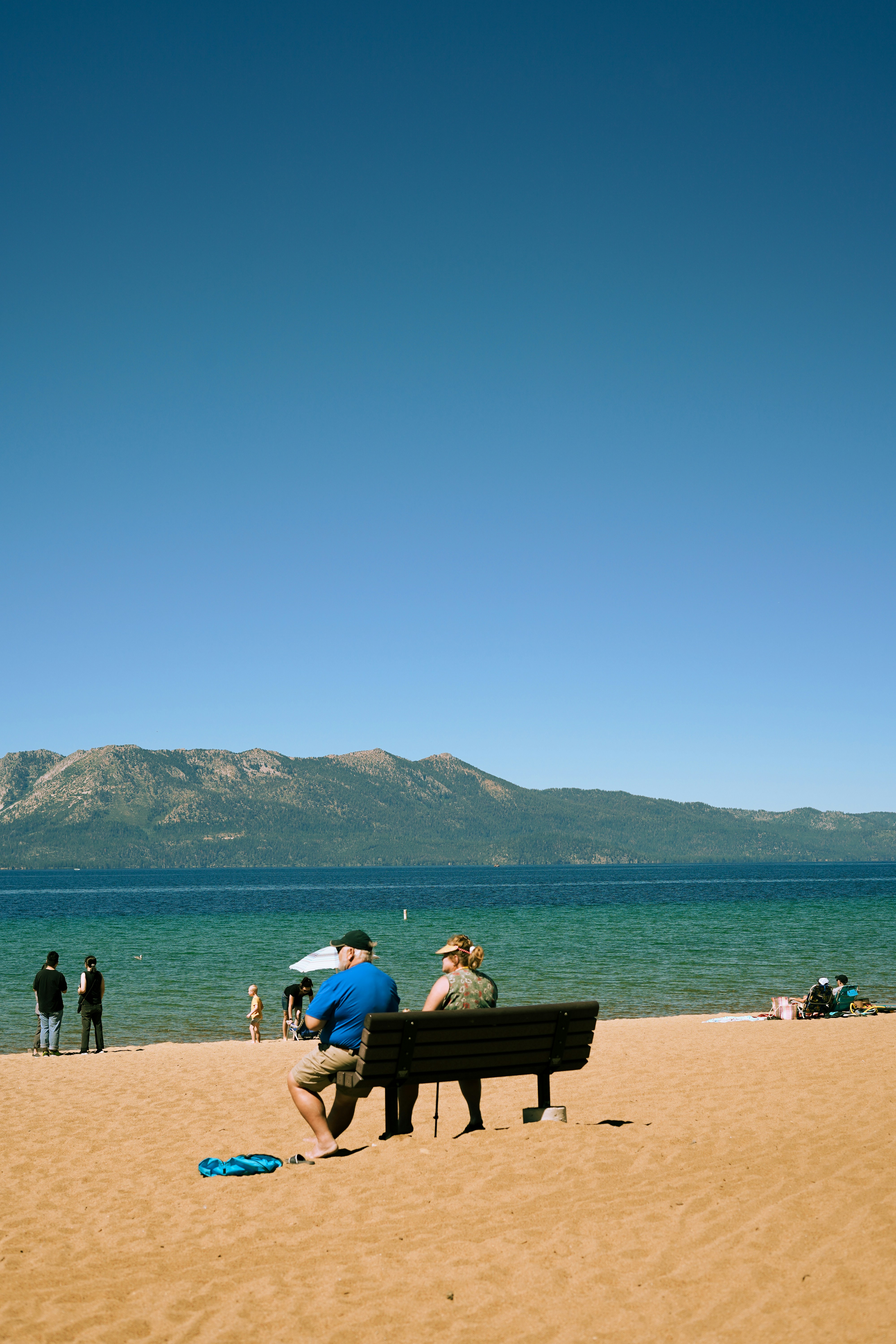 a man sitting on top of a bench on top of a sandy beach