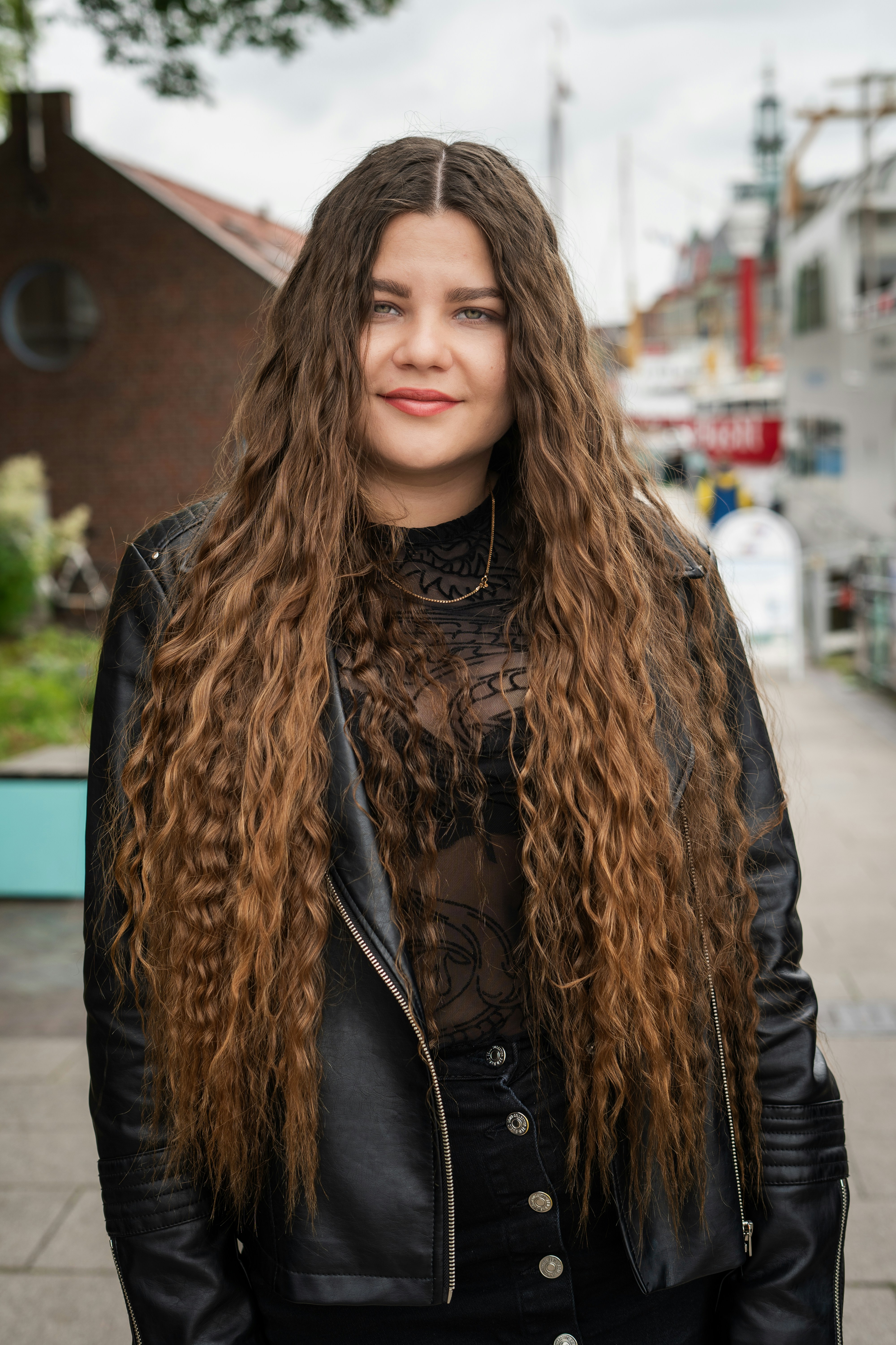 A woman with long hair standing on a sidewalk photo – Free Emden Image ...