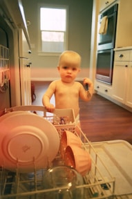a baby standing inside of a dishwasher in a kitchen