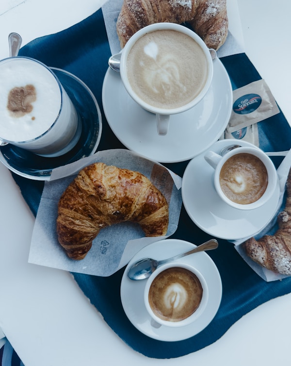 A table topped with cups of coffee and croissants