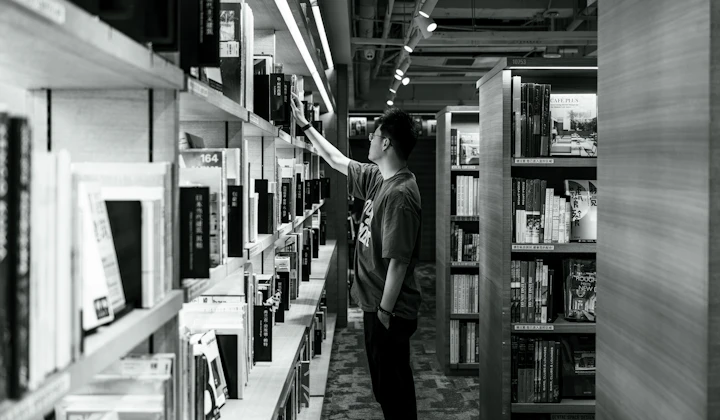 Persona consultando libros en una biblioteca para continuar su formación