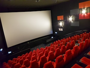 an empty theater with red seats and a projector screen
