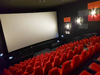 Empty theater with red seats facing a lit projector screen