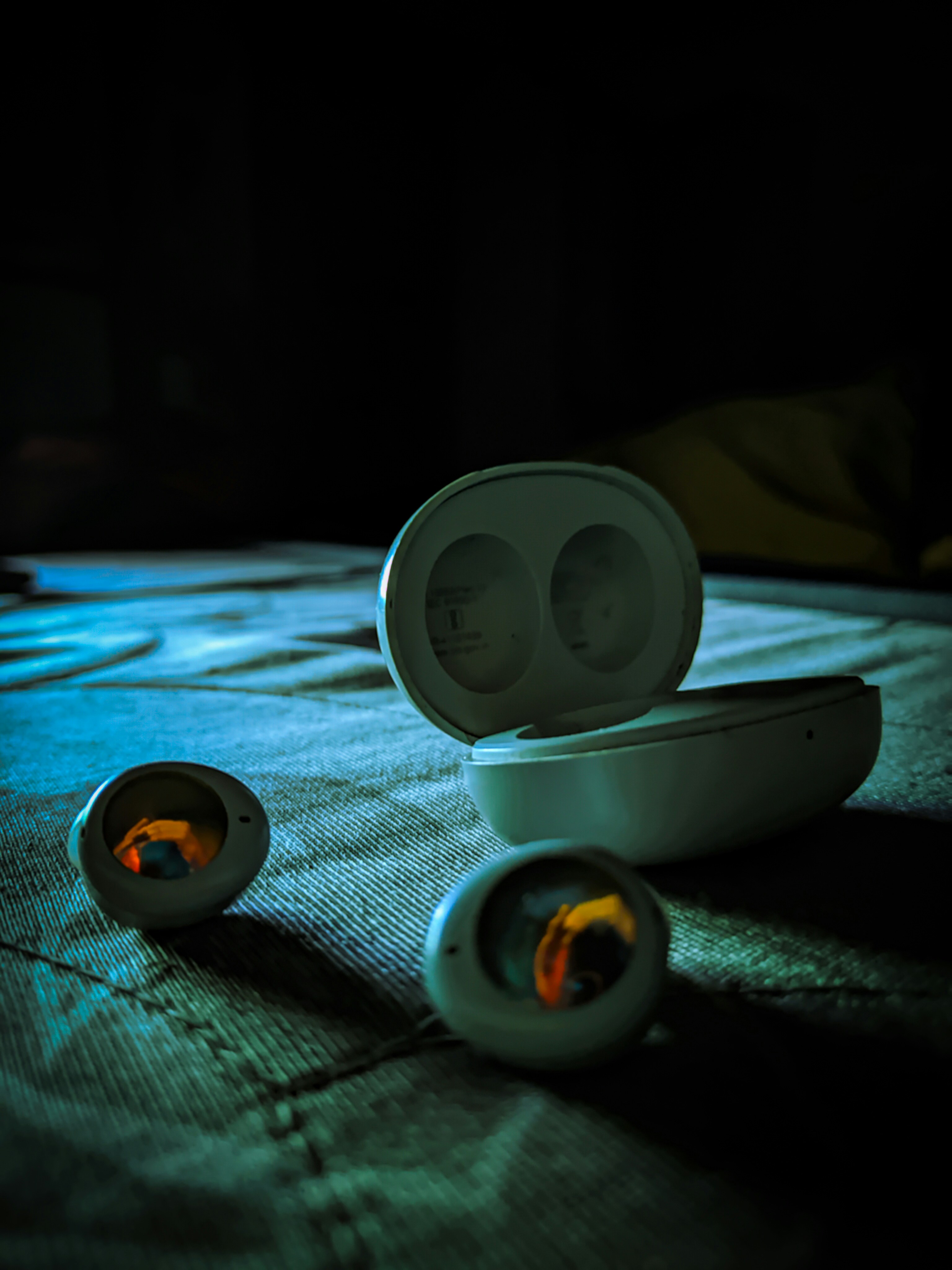 Premium wireless earbuds in charging case on dark matte surface, dim atmospheric lighting