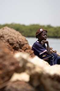 a young boy sitting on a rock next to a body of water