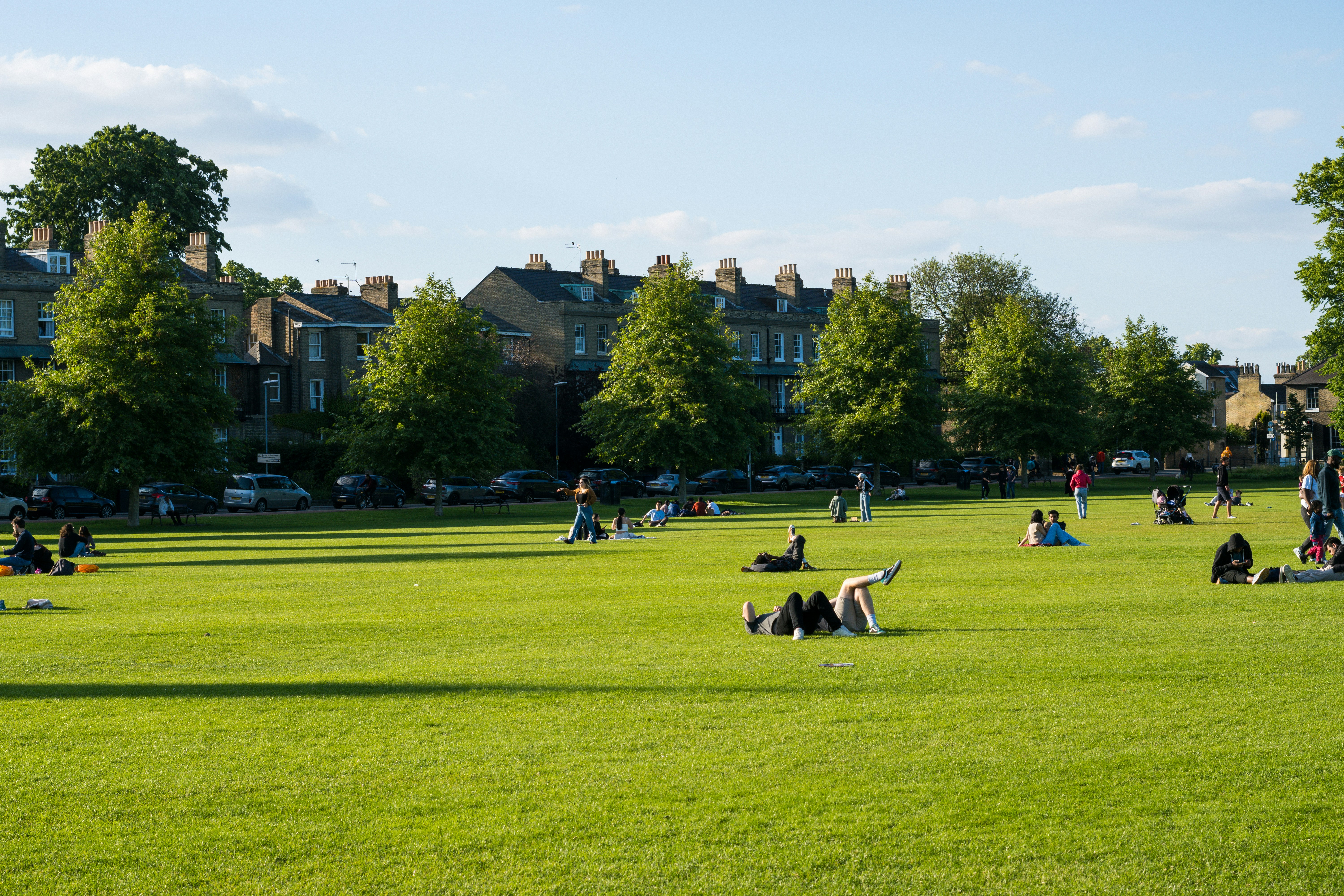 Children playing in a British park on a summer day, parent watching from a picnic blanket