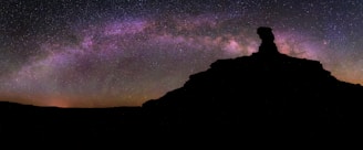 a person standing on top of a mountain under a night sky filled with stars