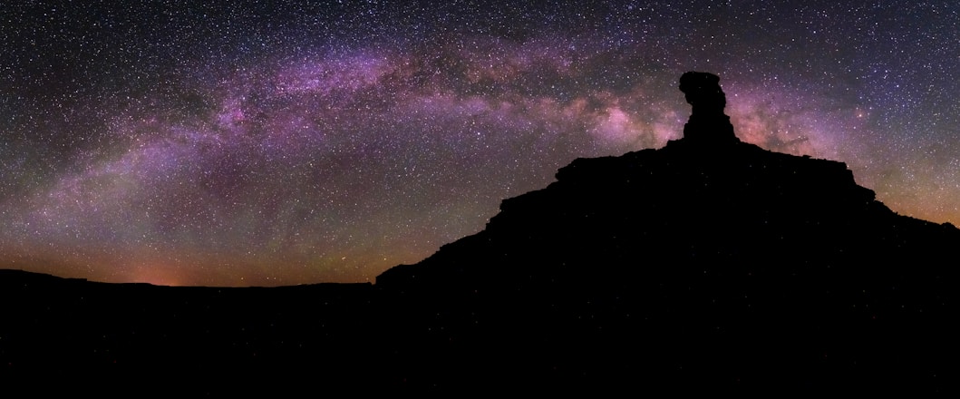 a person standing on top of a mountain under a night sky filled with stars