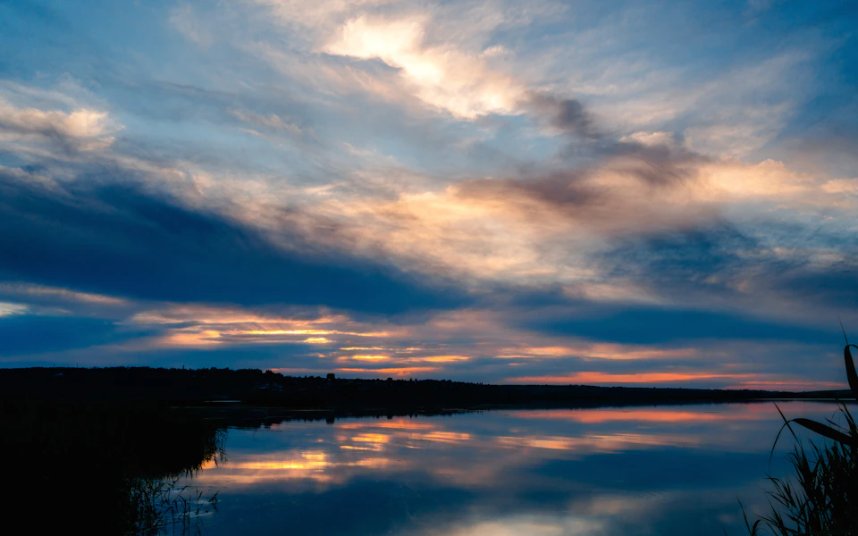 Serene lake at sunset with orange and blue hues, reflecting vibrant sky colors perfectly