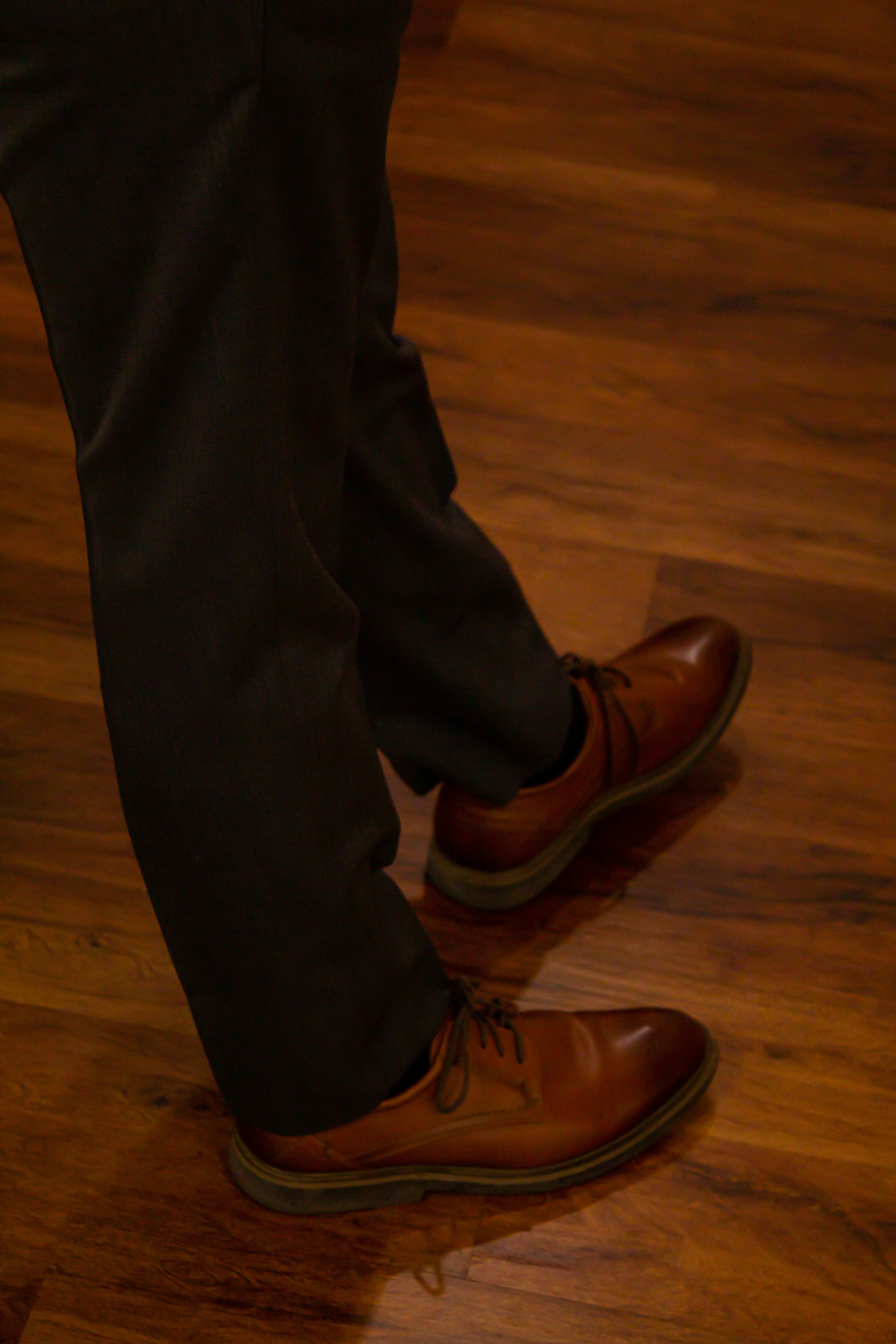 a person wearing brown shoes standing on a wooden floor