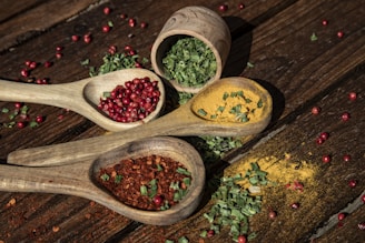 three wooden spoons filled with spices on top of a wooden table