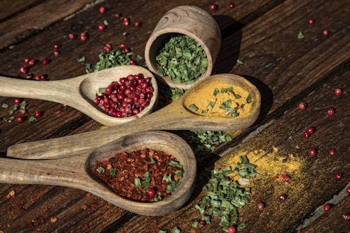 three wooden spoons filled with spices on top of a wooden table