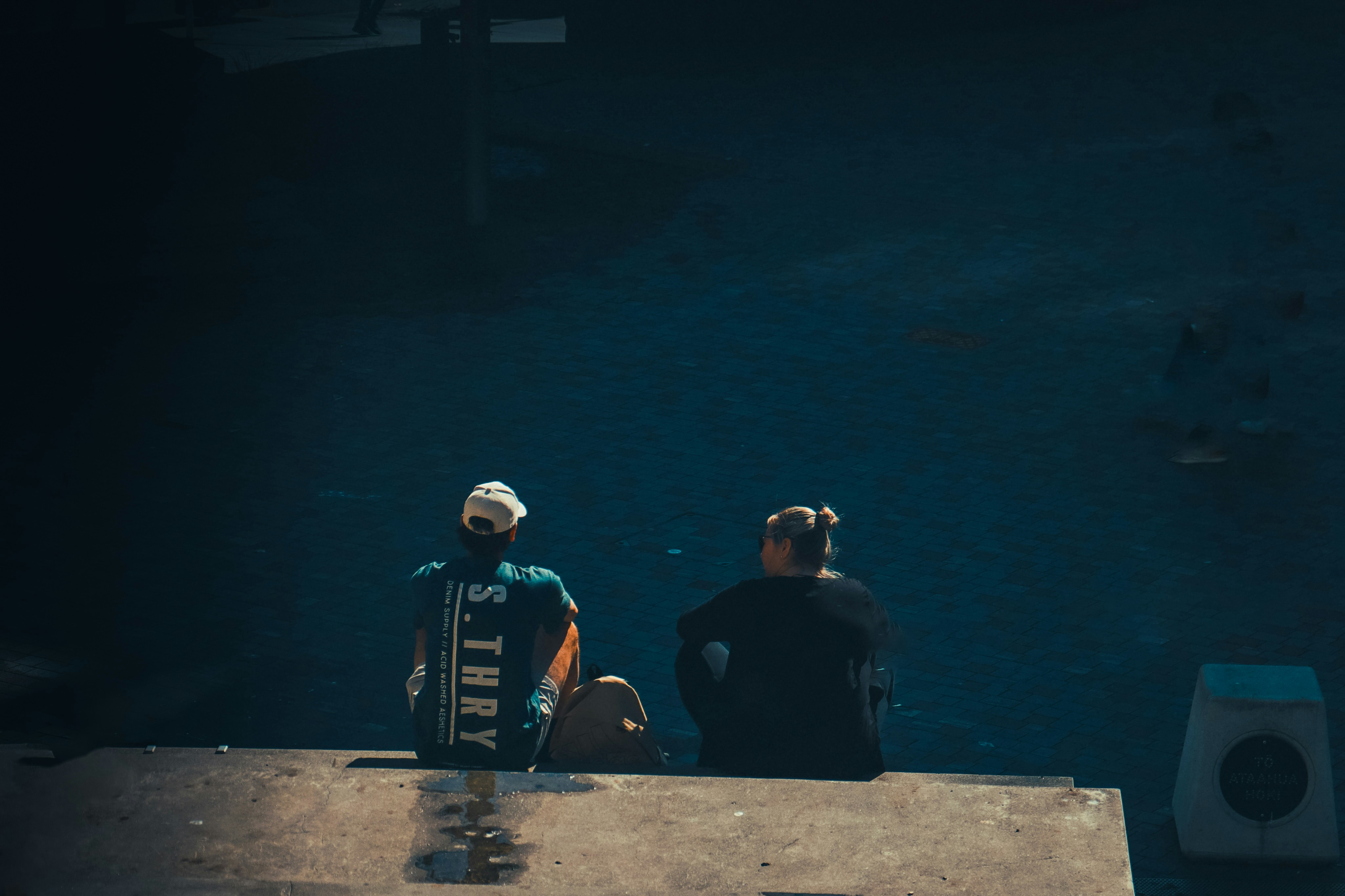 two people sitting on a ledge looking at the water