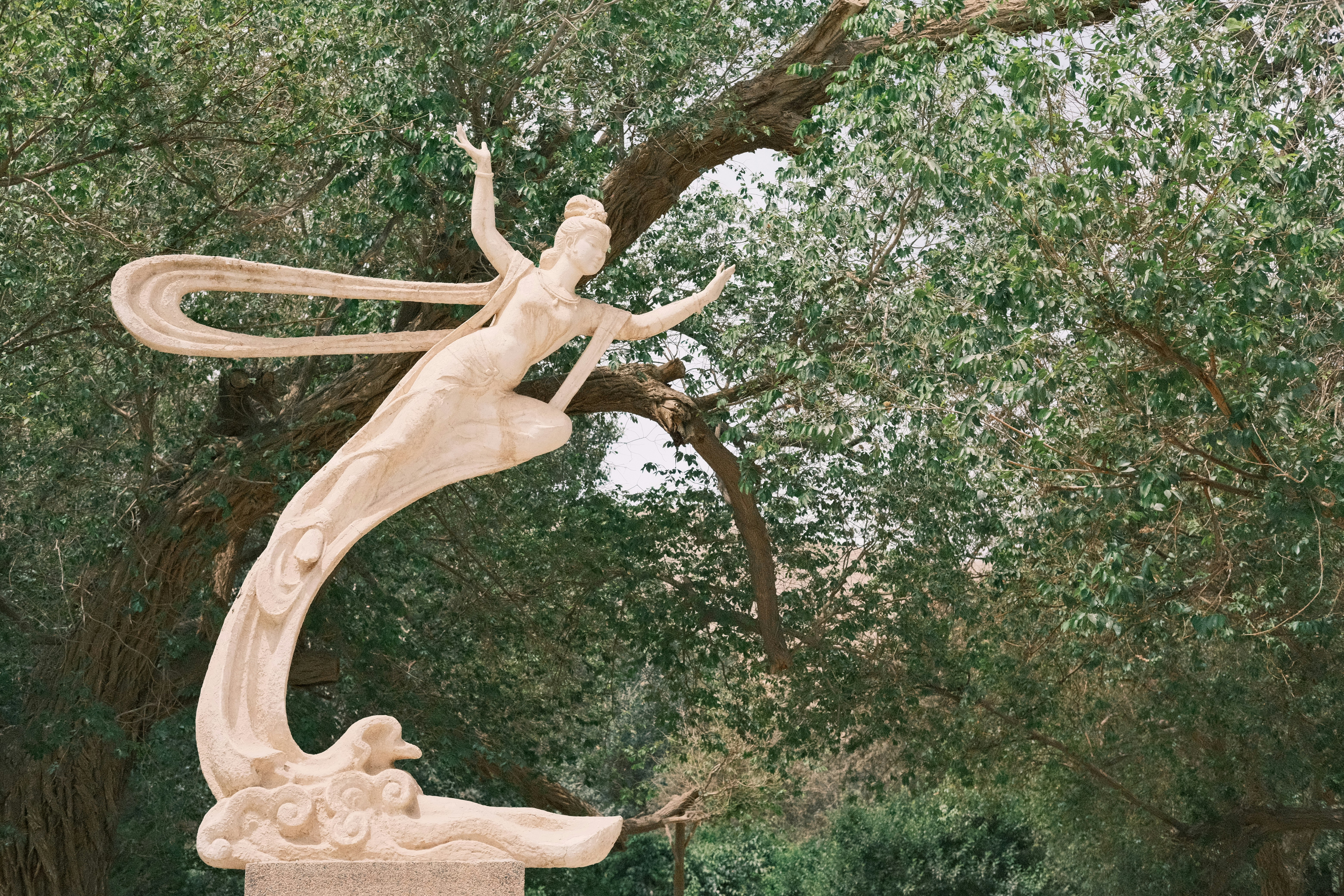 a statue of a woman holding a bird in a park