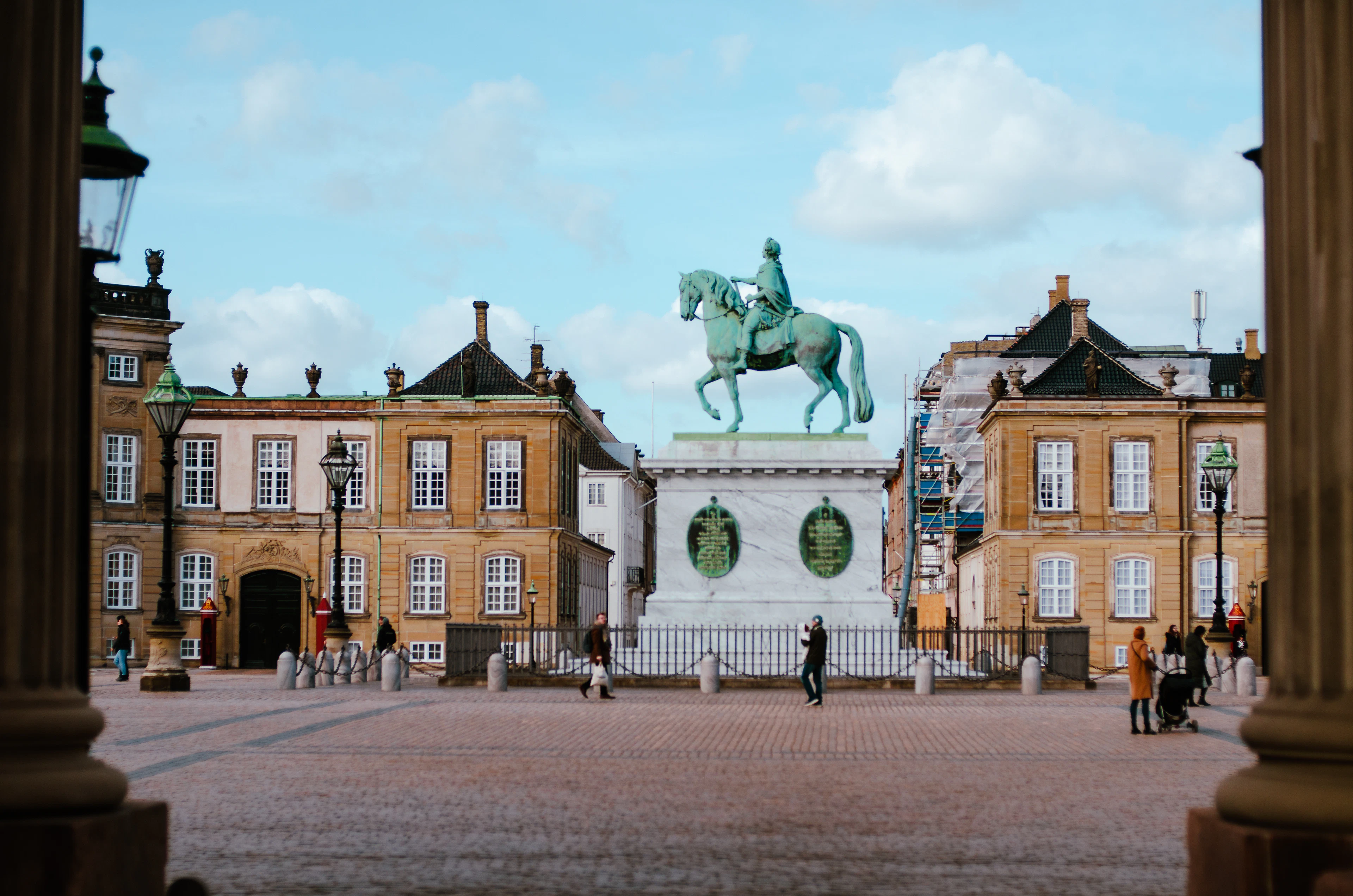 Amalienborg Palace Square in Copenhagen seen between two stone columns, the green equestrian statue of Frederik V on its plinth at the centre of the cobbled octagon, ringed by the rococo palaces