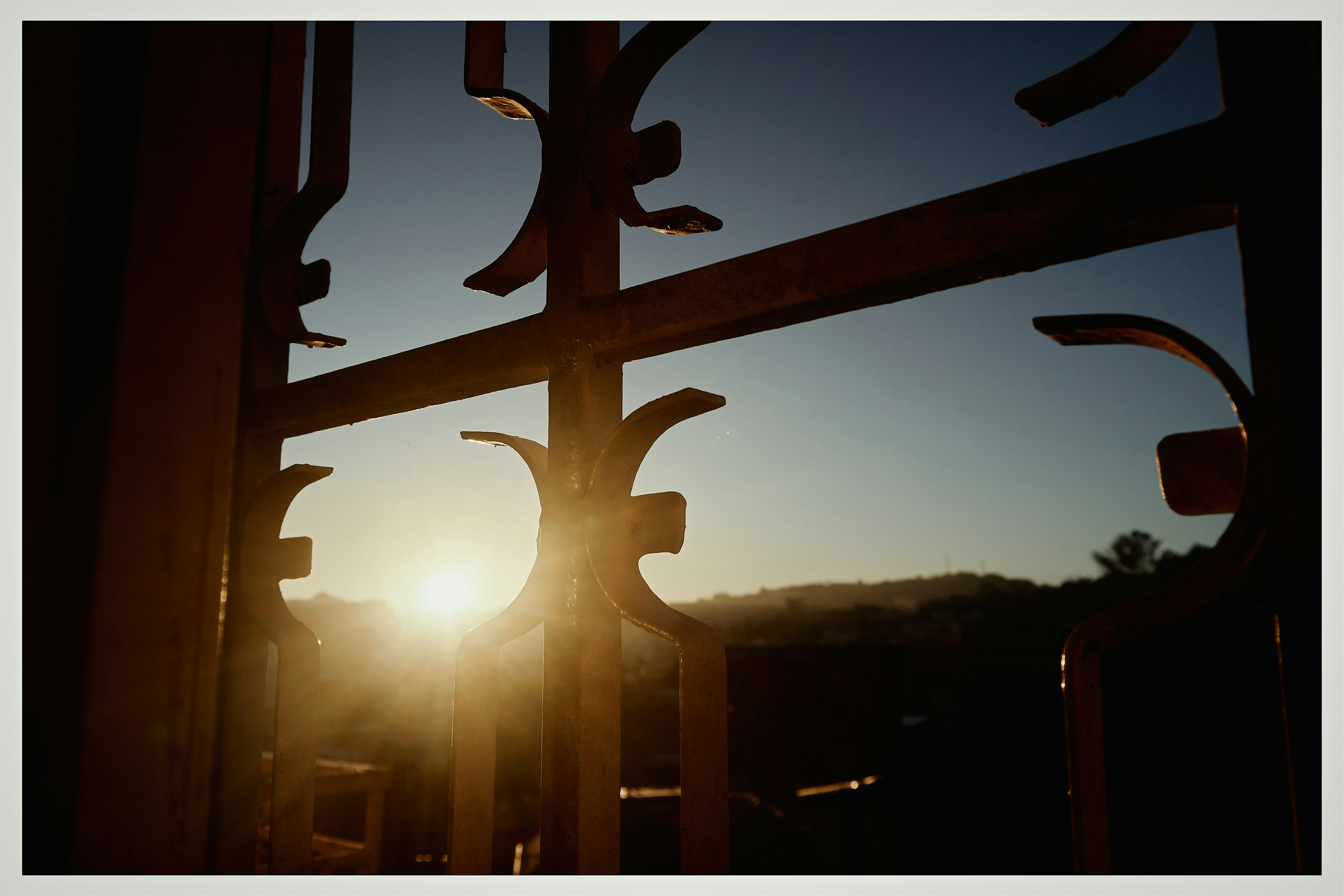 the sun is setting behind a metal gate