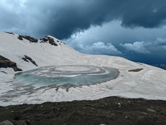 a snow covered mountain with a circular pool of water