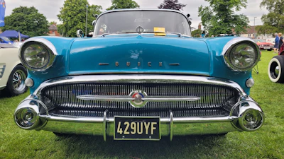 a blue classic car parked on top of a lush green field