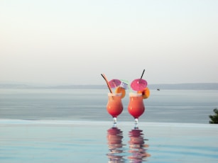 a couple of drinks sitting on top of a swimming pool