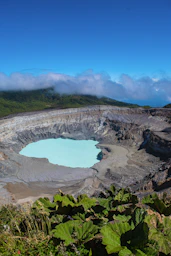 a large crater surrounded by green plants and clouds
