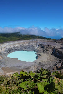 a large crater surrounded by green plants and clouds