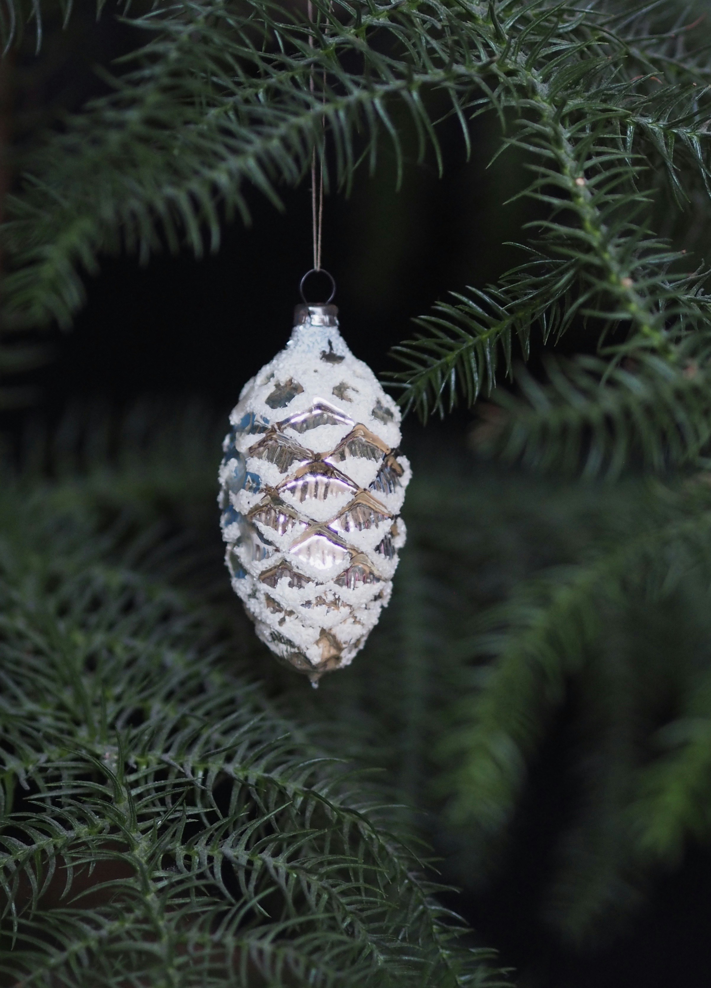a pine cone ornament hanging from a pine tree