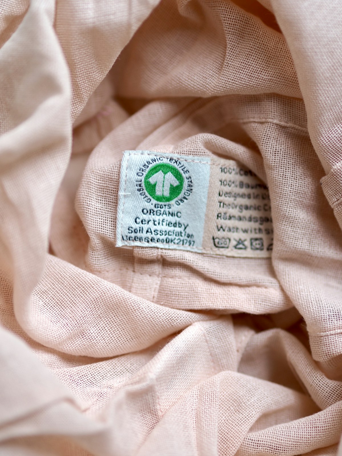 Primer plano de la etiqueta de cuidado de una prenda de algodón rosa, con la fila de símbolos de lavado, blanqueo, planchado y secado impresos junto al texto