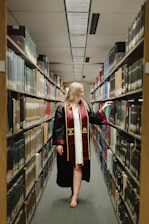 a woman in a graduation gown is walking through a library