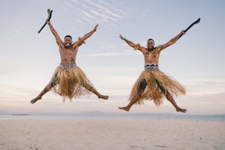 two men in grass skirts jumping in the air