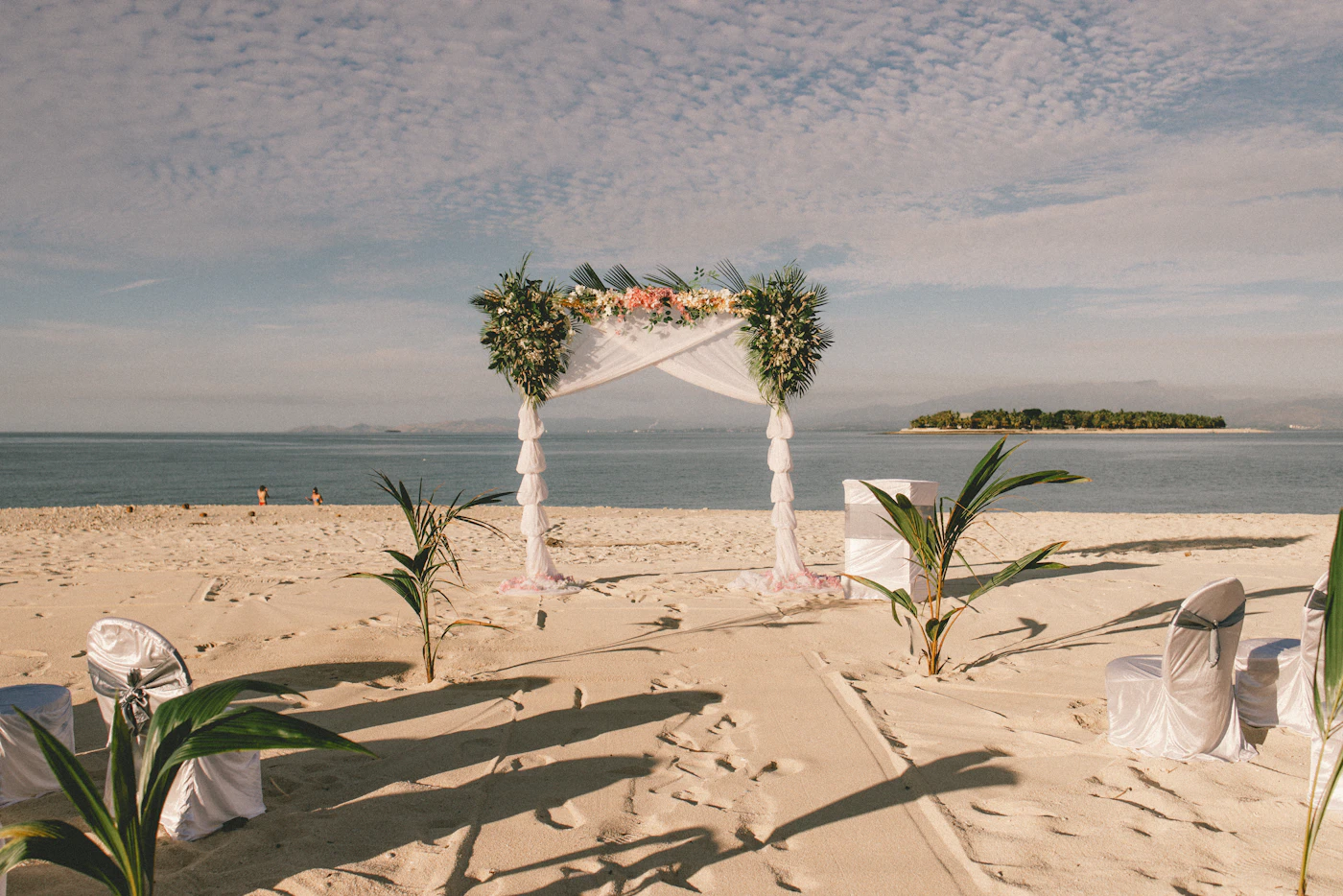 Bridal jumpsuits for non-traditional beach weddings — A bride in a wide-leg jumpsuit walking barefoot on a sandy beach