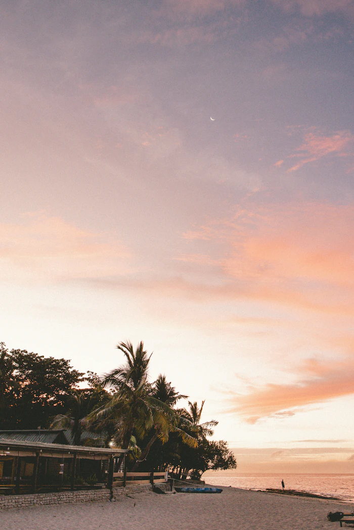 A few people spread out along a sandy beach at sunset on Beachcomber Island, Fiji