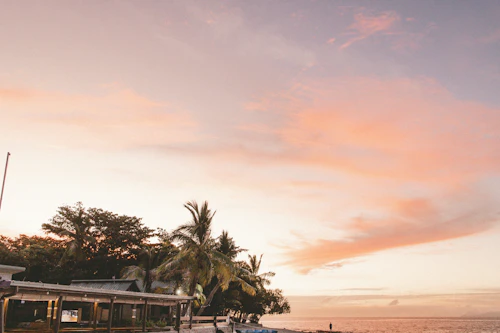 A boat pulled up on the sand of a Fiji beach at sunset with pink light over the water